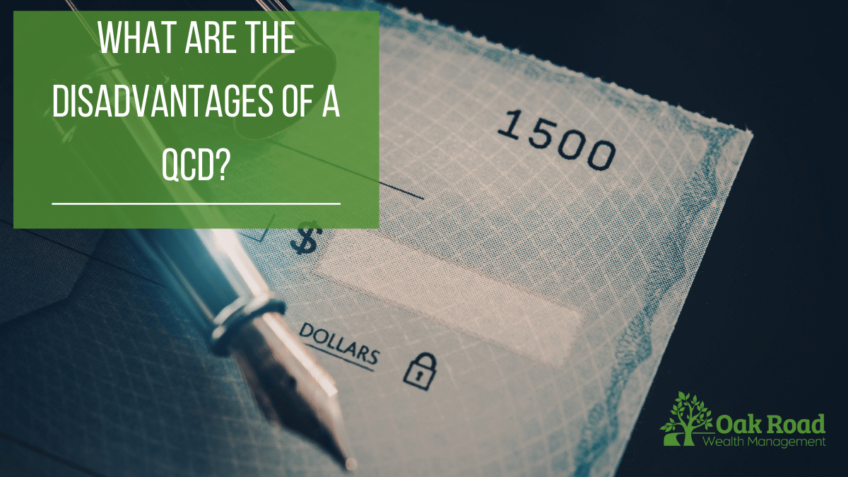 A fountain pen resting on a check with a green overlay reading "What are the Disadvantages of a QCD?" and the Oak Road Wealth Management logo.